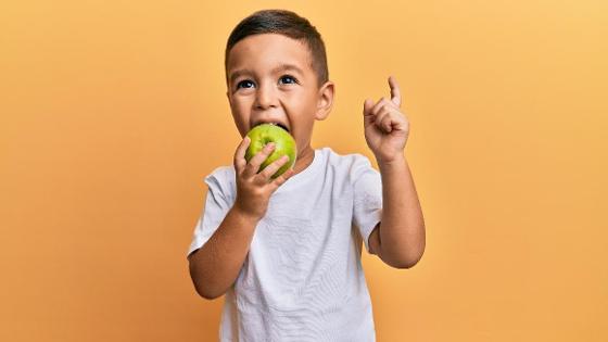 Ein Junge isst einen Apfel und hebt den Finger