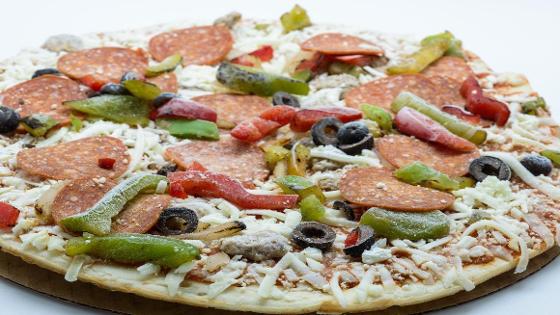 Tiefkühlpizza, belegt mit Paprikastücken, Salami, Oliven und Käse in tiefgerorenem Zustand
